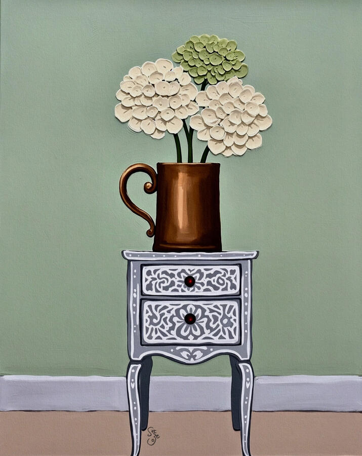 Cream and lime hydrangea flowers in a brown iron jar sitting atop a white patterned light grey vintage inlaid cabinet. Dusty sage background.