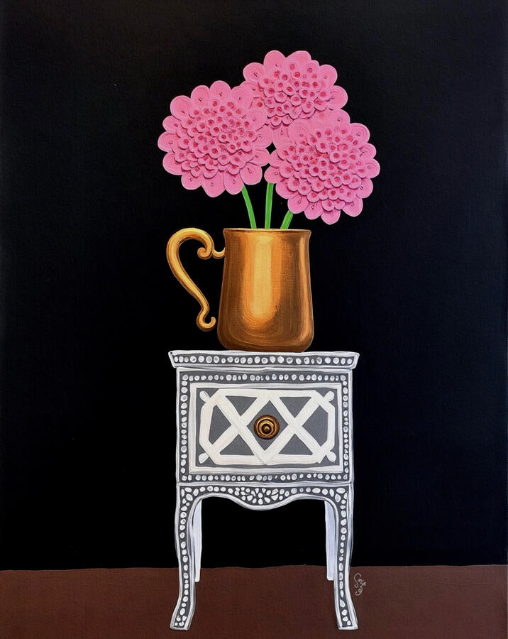 Pink tactile hydrangea flowers in a golden jar sitting atop a white patterned grey vintage inlaid cabinet. Black wall background.