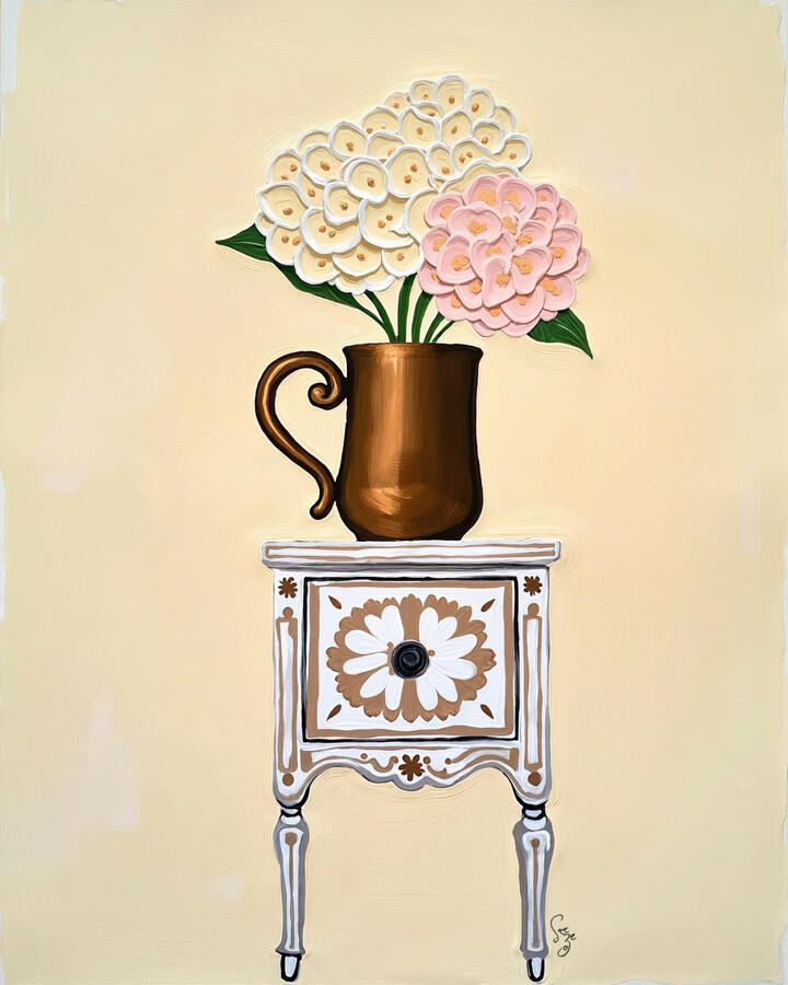 Blush and Cream hydrangea flowers in an antique bronze jar sitting atop a white patterned light brown vintage inlaid cabinet. Off white background.