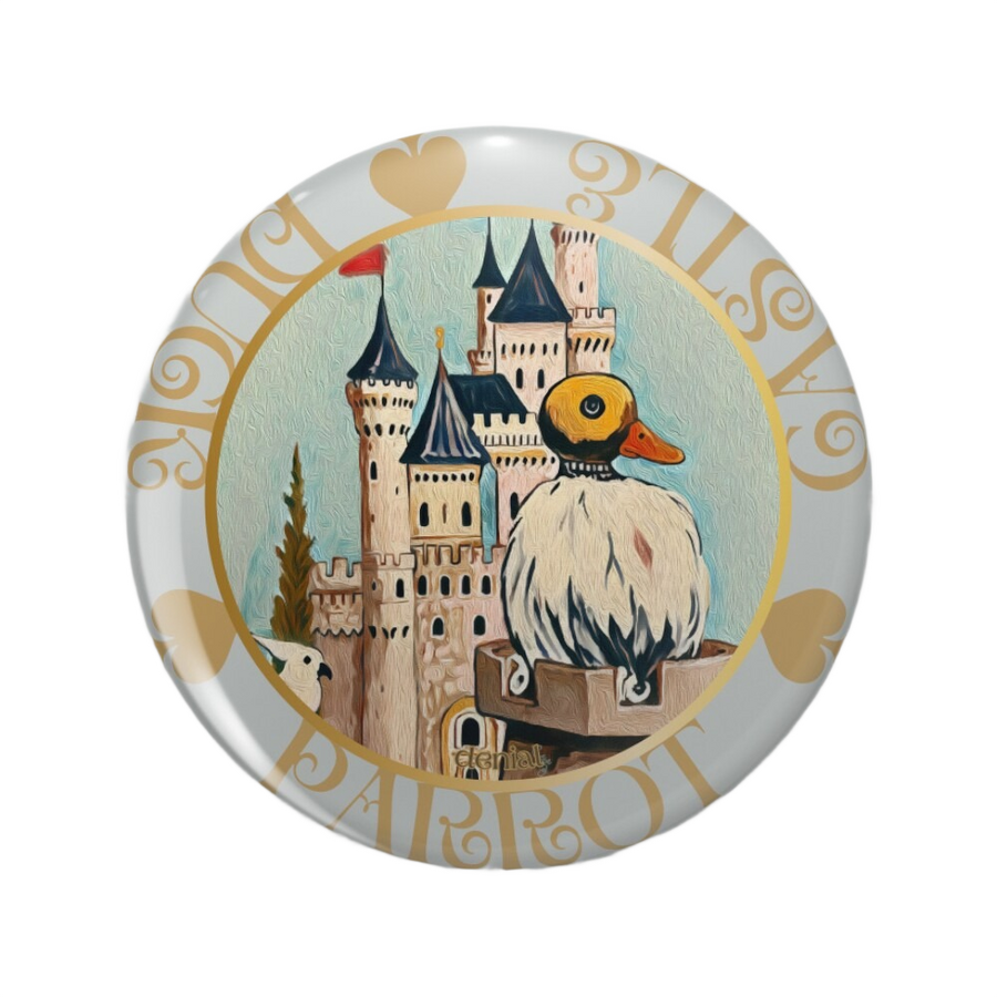 An ornate round pinback button close up, containing an illustration of A vintage-style illustrated card titled “Shy,” showing a duck-like robot and a pink parrot before a medieval castle.