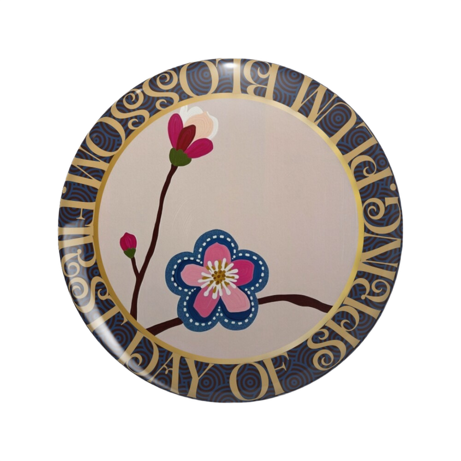 An ornate round pink back button close up, containing an illustration of a pink blossom with stitched denim edges. Hover Text reads “Visit Redbubble to collect the Pin Button"