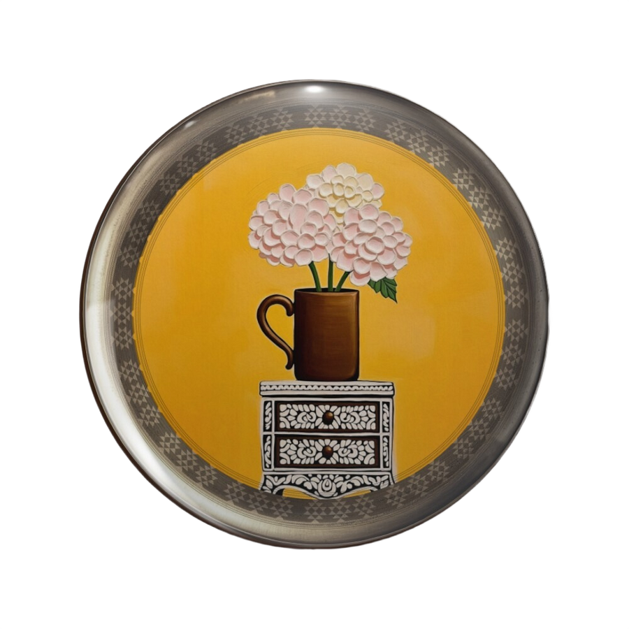 An ornate round pinback button close up, containing a patterned inlay vintage cabinet and tactile pastel hydrangea flowers, against bright yellow wall.