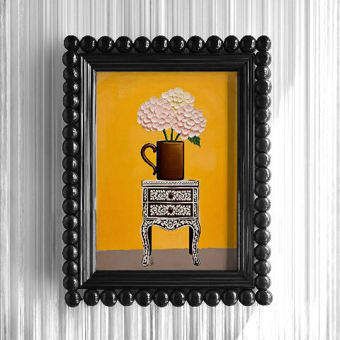 A piece of art showing a patterned inlay vintage cabinet and hydrangea flowers, framed by a dark, beaded decorative border on striped white wall.