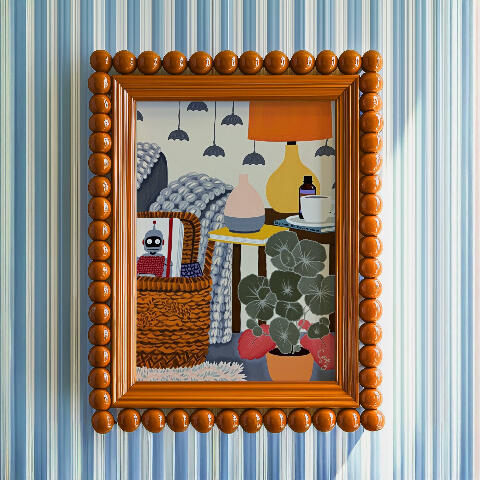 Framed mockup of a cozy interior still life with a woven chair, robot book, diffuser, lamp, coffee cup, plant, and orange bubble bead frame.