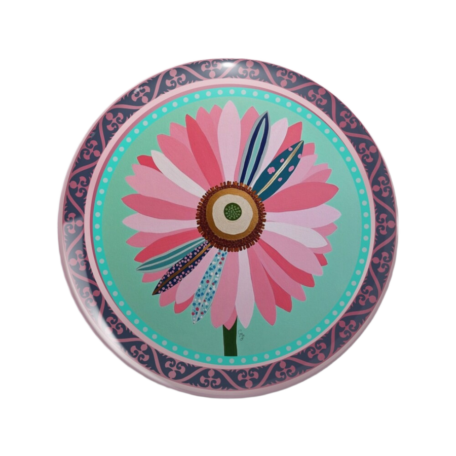 An ornate round pinback button close up, containing an illustration of a pink flower’s circular center with layered pink petals and patterned teal and blue petal details.
